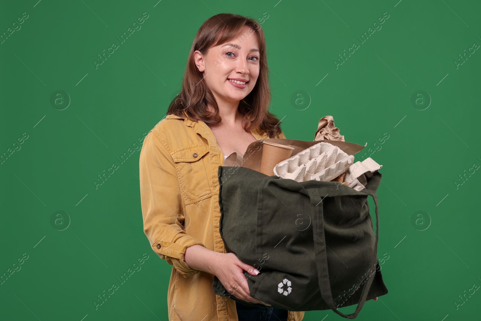Photo of Recycling. Smiling woman with bag full of different waste paper on green background