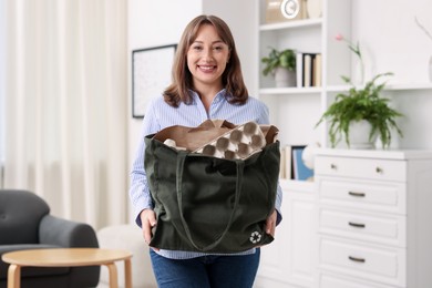 Photo of Recycling. Smiling woman with bag full of different waste paper indoors