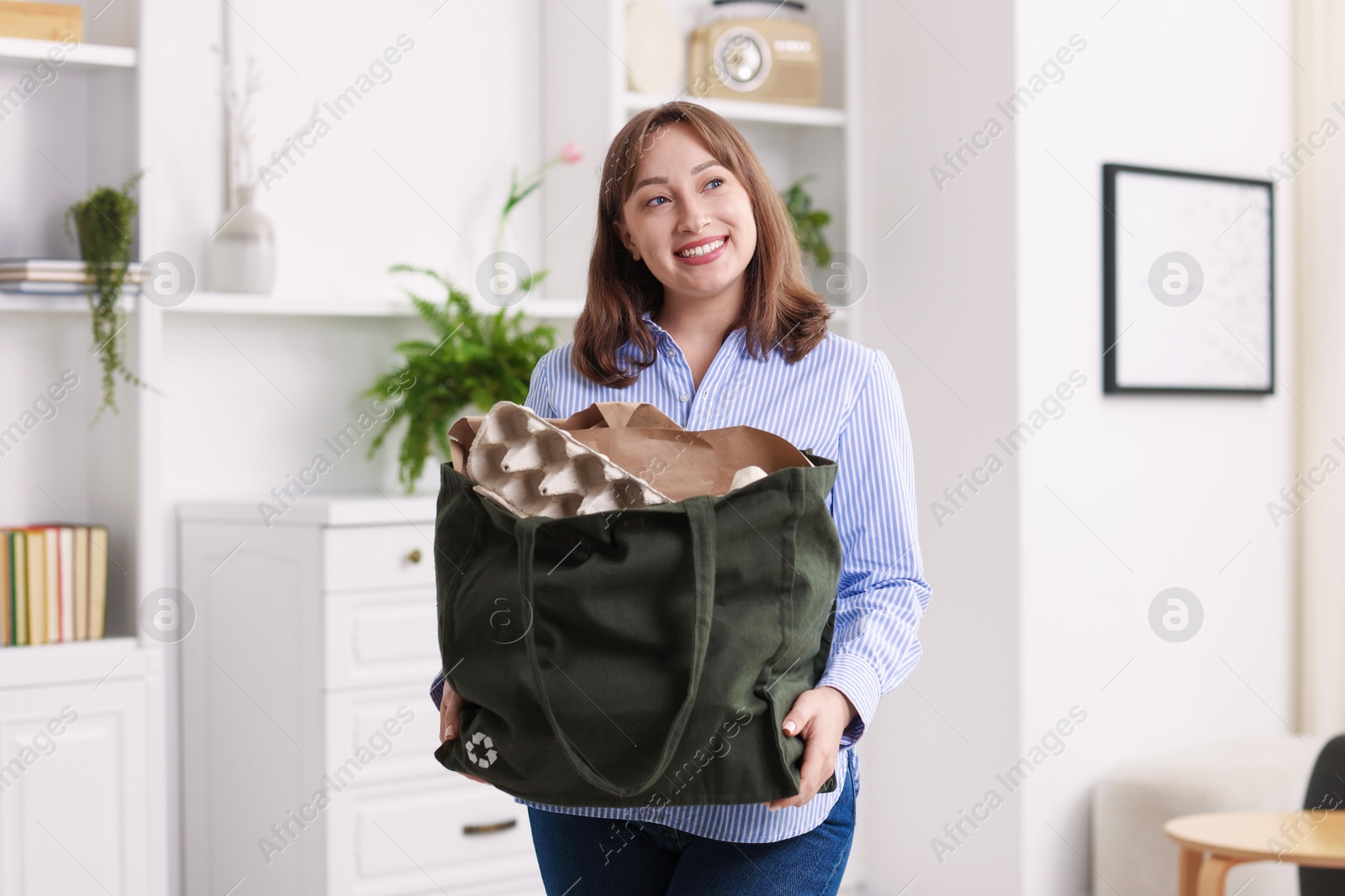 Photo of Recycling. Smiling woman with bag full of different waste paper indoors