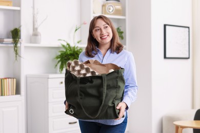 Photo of Recycling. Smiling woman with bag full of different waste paper indoors