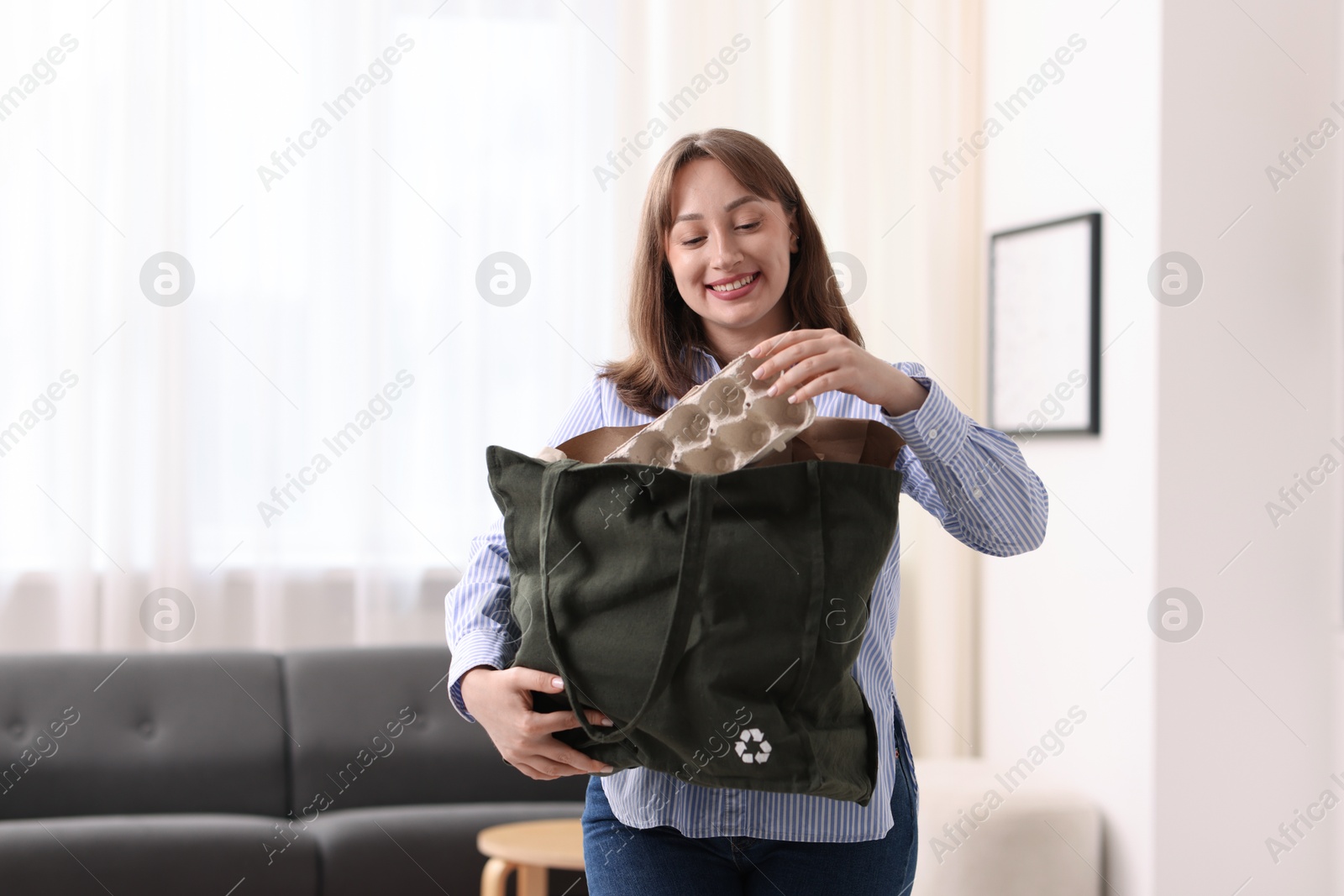 Photo of Recycling. Smiling woman with bag full of different waste paper indoors