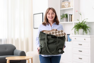 Photo of Recycling. Smiling woman with bag full of different waste paper indoors