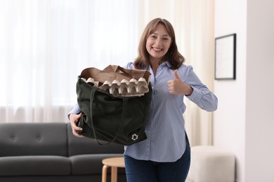 Photo of Recycling. Smiling woman with bag full of different waste paper showing thumbs up indoors