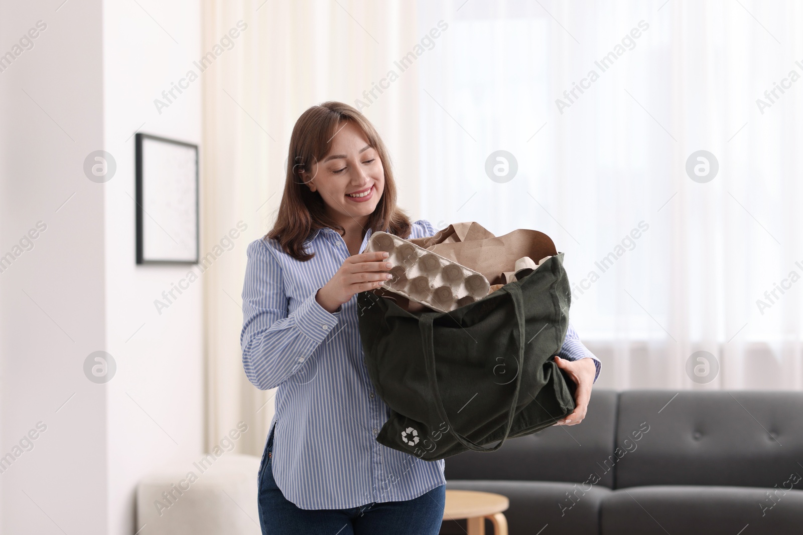 Photo of Recycling. Smiling woman with bag full of different waste paper indoors