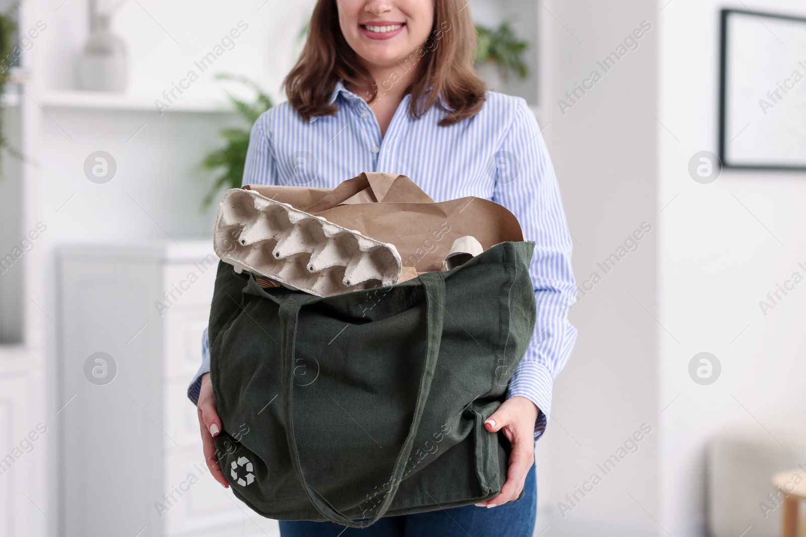 Photo of Recycling. Smiling woman with bag full of different waste paper indoors, closeup