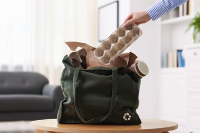 Photo of Recycling. Woman putting waste paper into bag at wooden table indoors, closeup