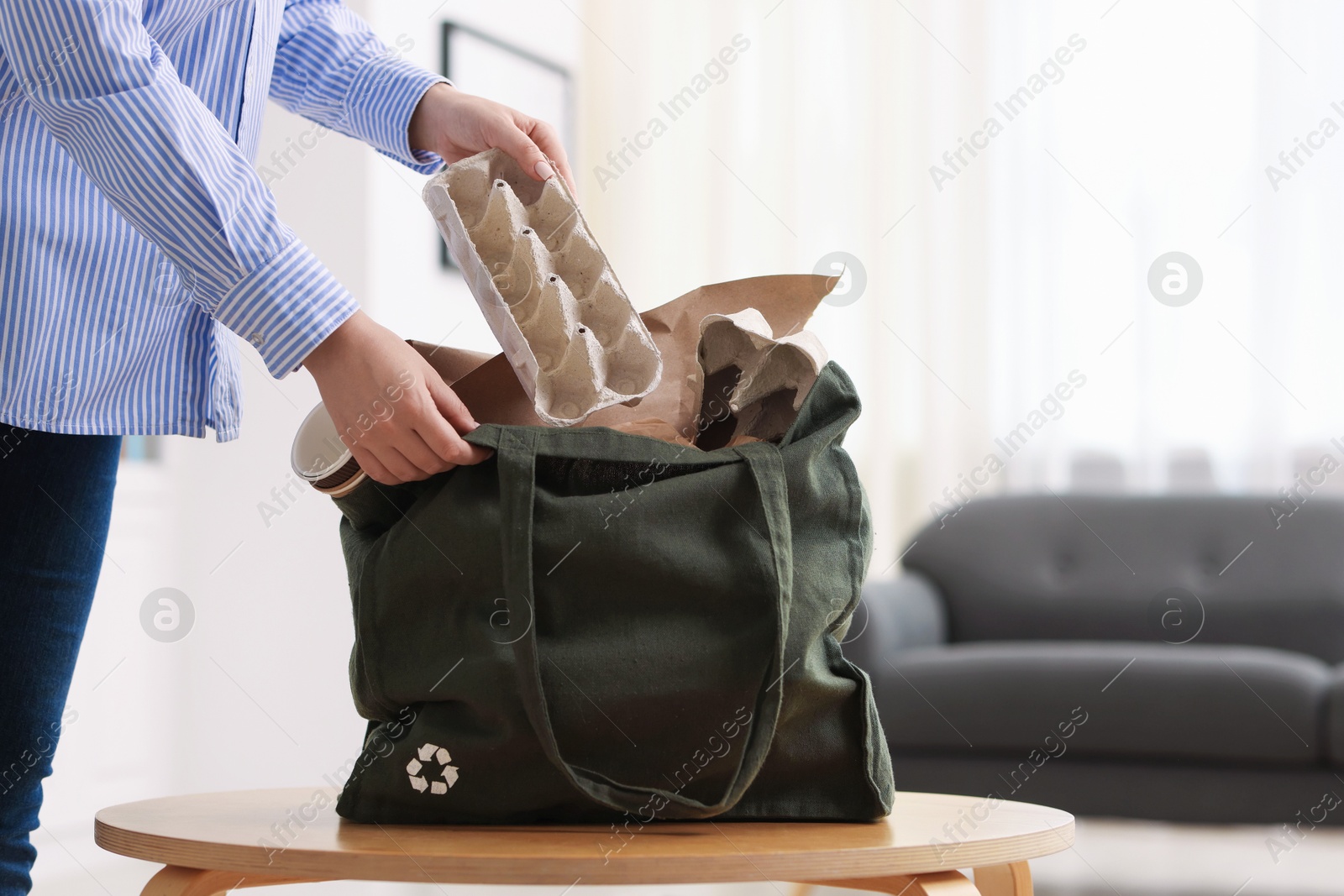 Photo of Recycling. Woman putting waste paper into bag at wooden table indoors, closeup