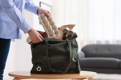 Photo of Recycling. Woman putting waste paper into bag at wooden table indoors, closeup