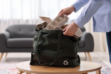 Photo of Recycling. Woman putting waste paper into bag at wooden table indoors, closeup