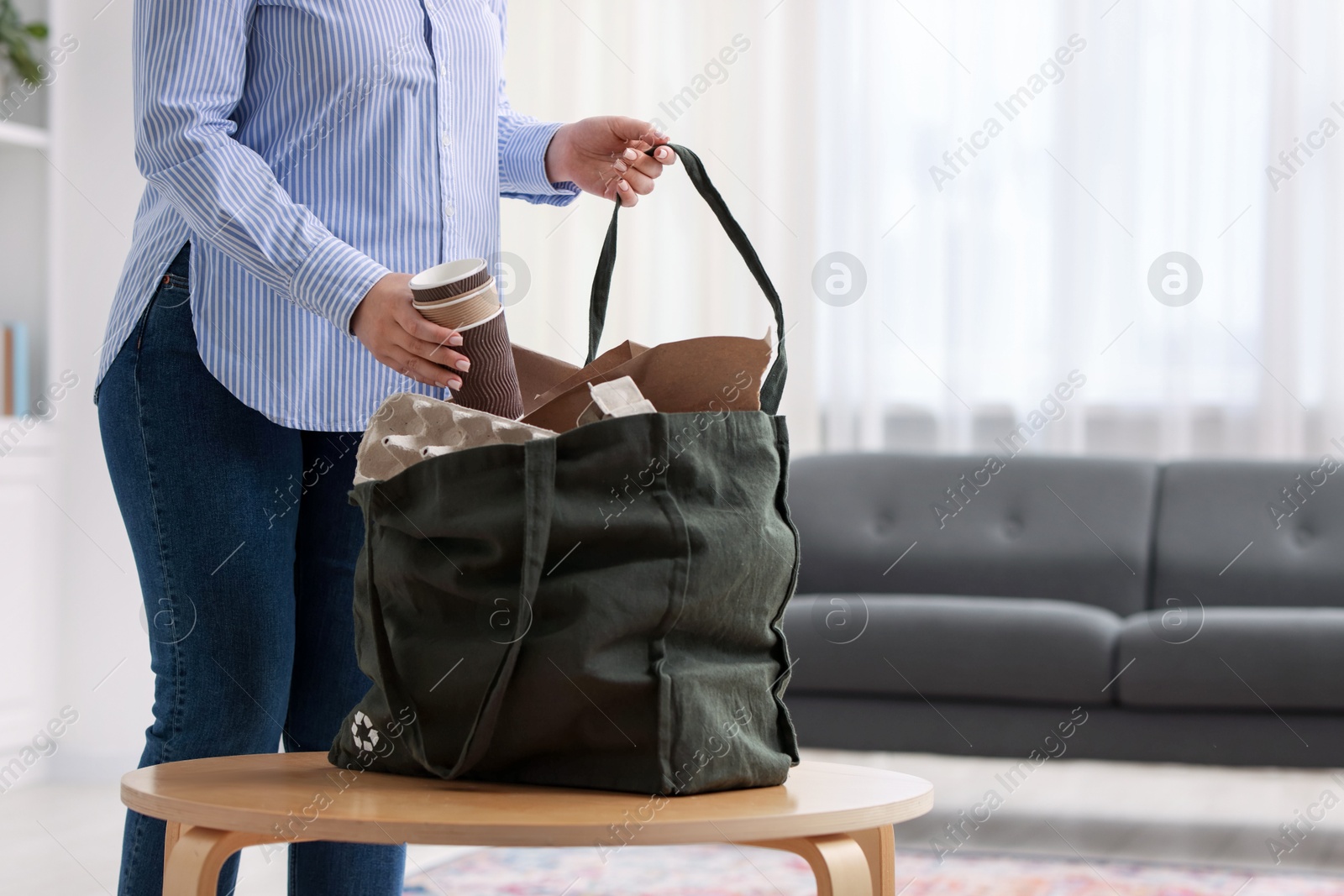 Photo of Recycling. Woman putting waste paper into bag at wooden table indoors, closeup