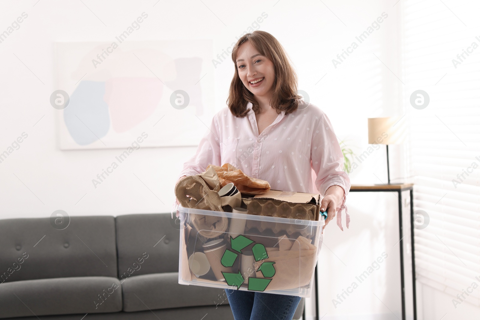 Photo of Recycling. Smiling woman holding plastic box with different waste paper indoors