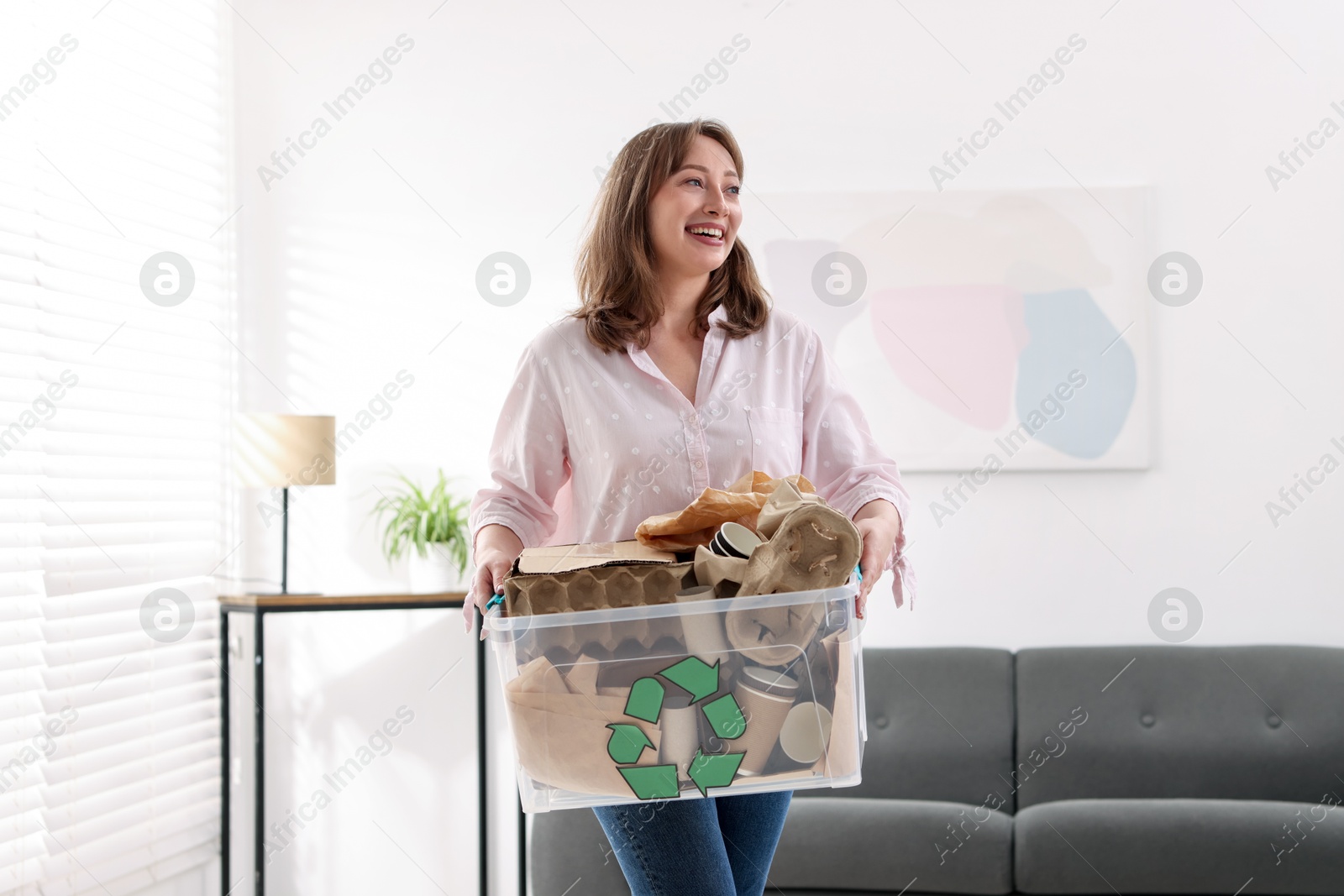 Photo of Recycling. Smiling woman holding plastic box with different waste paper indoors