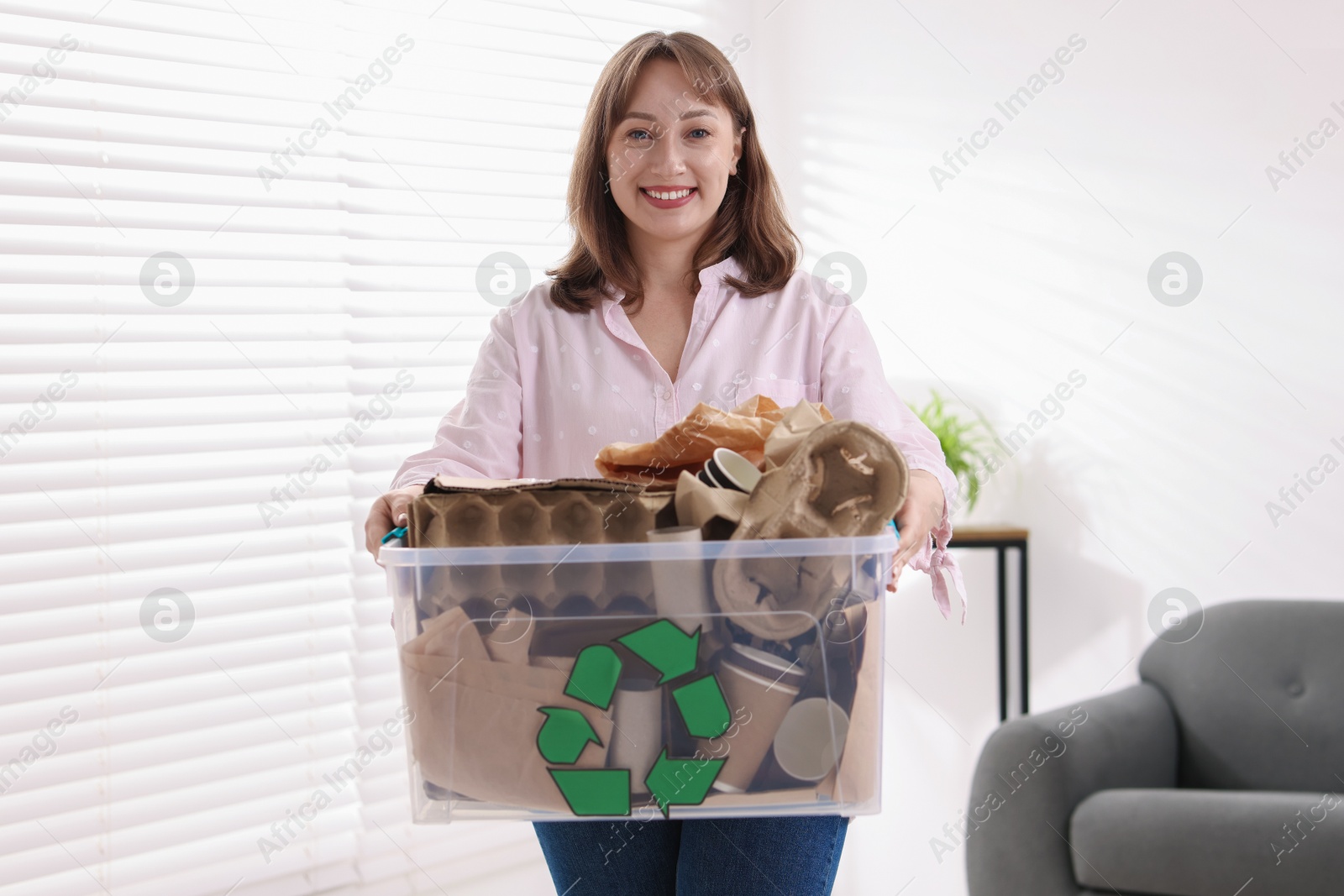 Photo of Recycling. Smiling woman holding plastic box with different waste paper indoors