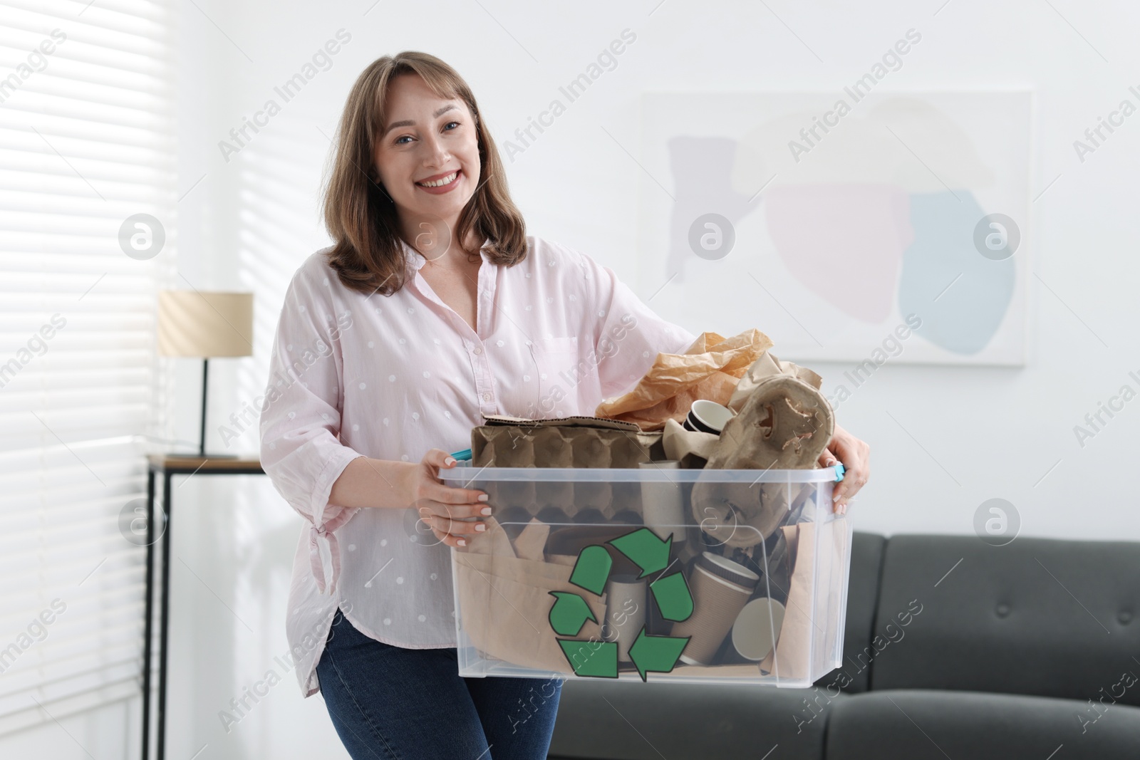 Photo of Recycling. Smiling woman holding plastic box with different waste paper indoors