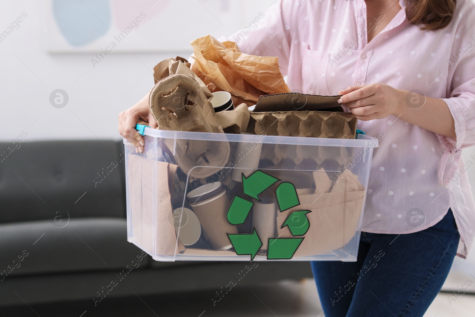 Photo of Recycling. Woman holding plastic box with different waste paper indoors, closeup