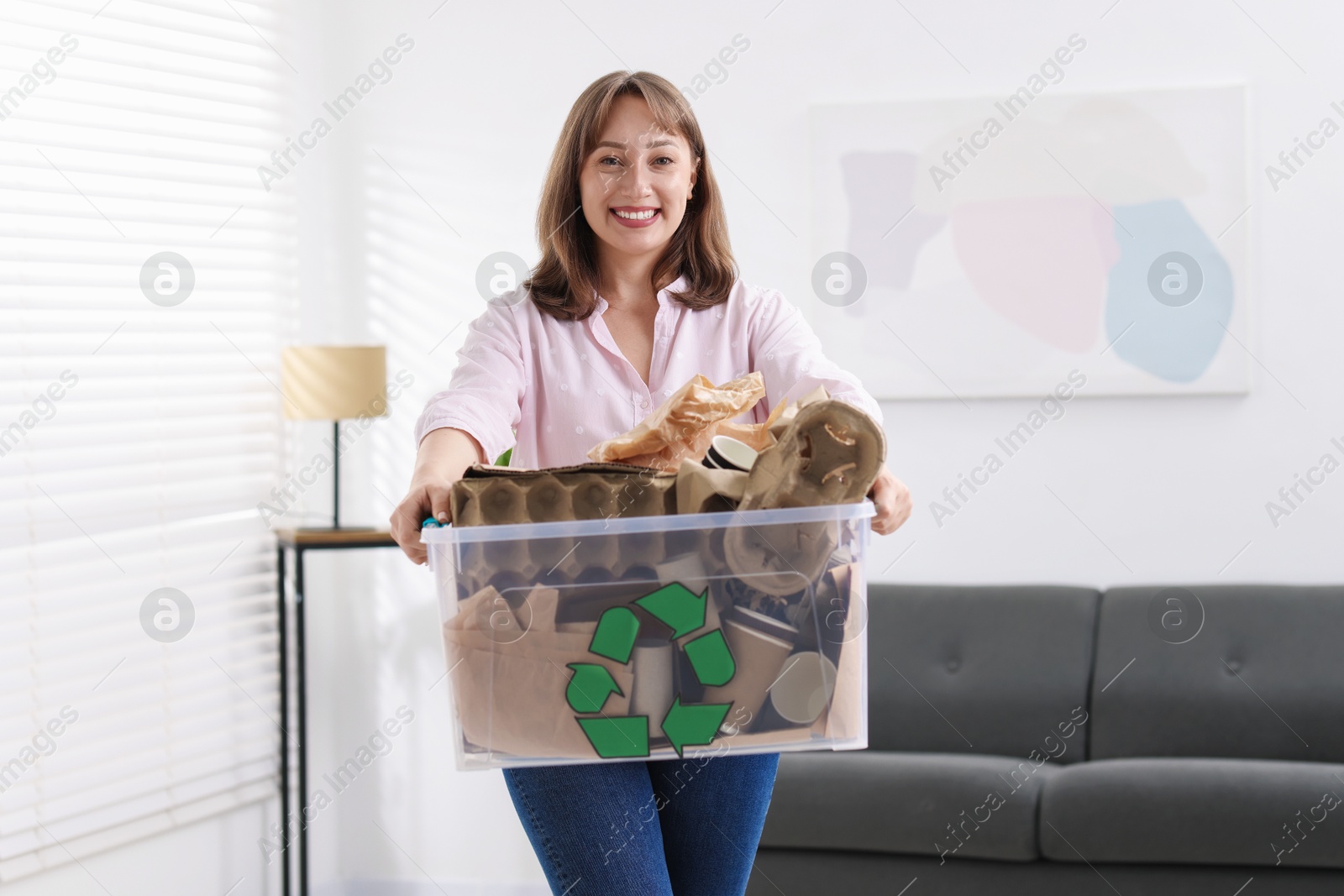 Photo of Recycling. Smiling woman holding plastic box with different waste paper indoors