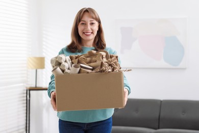 Photo of Recycling. Smiling woman holding cardboard box with different waste paper indoors