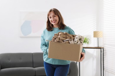 Photo of Recycling. Smiling woman holding cardboard box with different waste paper indoors