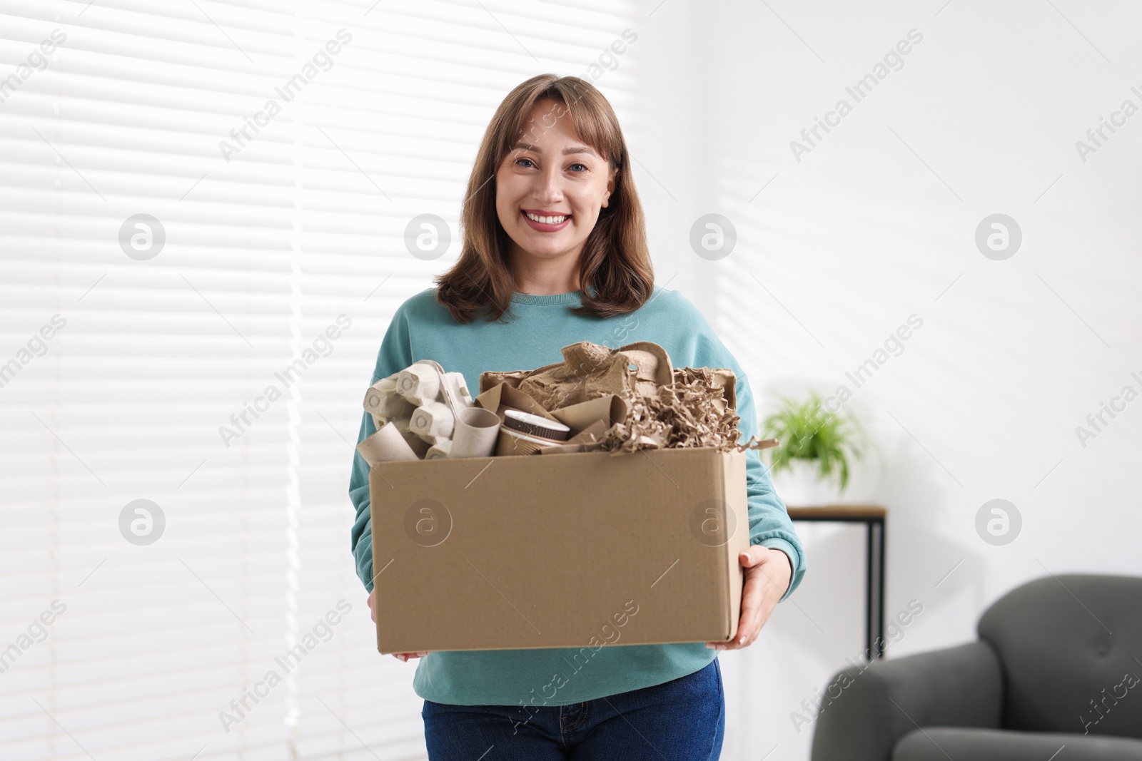 Recycling. Smiling woman holding cardboard box with different waste paper indoors Photo of Recycling. Smiling woman holding cardboard box with different waste paper indoors