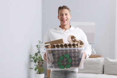 Photo of Recycling. Smiling man holding plastic box with different waste paper indoors