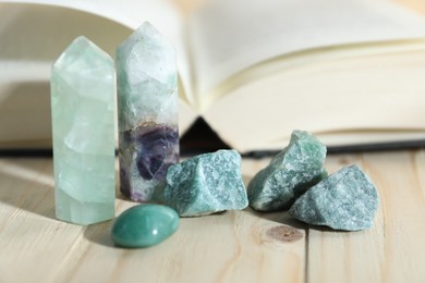 Photo of Different healing stones and book on wooden table, closeup