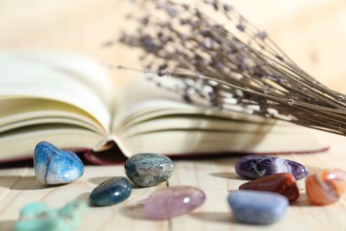 Photo of Different healing stones, book and lavender on wooden table, closeup