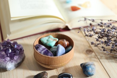 Photo of Different healing stones, book and lavender on wooden table, closeup