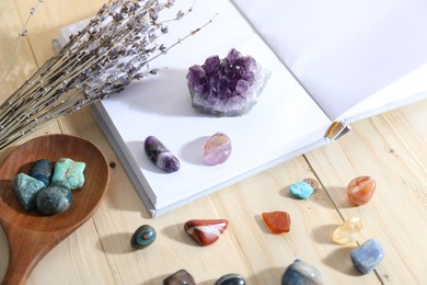 Photo of Different healing stones, book and lavender on wooden table, closeup