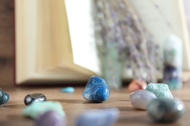 Photo of Different healing stones and book on wooden table, closeup