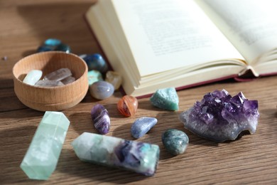 Photo of Different healing stones and book on wooden table, closeup