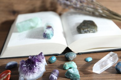 Photo of Different healing stones and book on wooden table, closeup