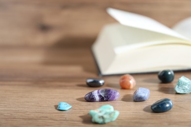 Photo of Different healing stones and book on wooden table, closeup. Space for text