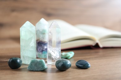 Photo of Different healing stones and book on wooden table, closeup