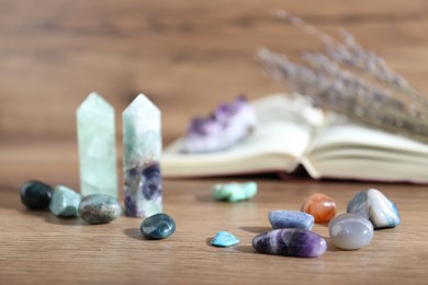 Photo of Different healing stones and book on wooden table, closeup