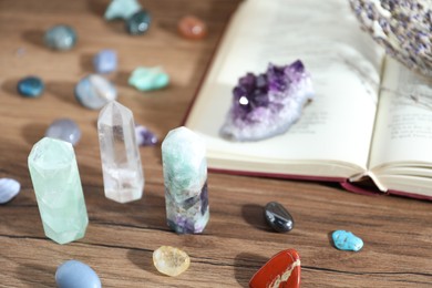 Photo of Different healing stones and book on wooden table, closeup