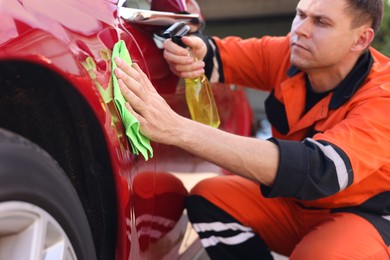 Photo of Man wiping car with green microfiber rag outdoors
