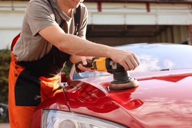 Photo of Man polishing car hood with orbital polisher outdoors, closeup