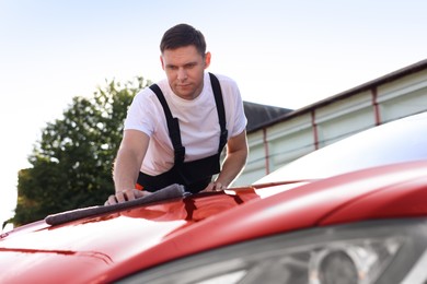 Photo of Man wiping car hood with grey microfiber rag outdoors