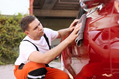Photo of Man wiping car with grey microfiber rag outdoors