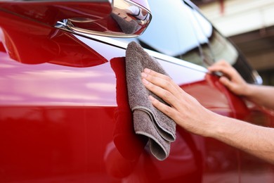 Photo of Man wiping car with grey microfiber rag outdoors, closeup