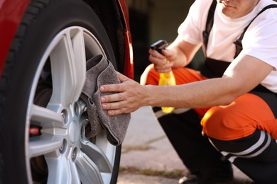 Photo of Man wiping car wheel with grey microfiber rag outdoors, closeup