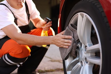 Photo of Man wiping car wheel with grey microfiber rag outdoors, closeup