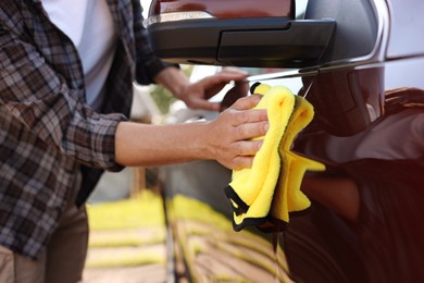 Photo of Man wiping car with yellow microfiber rag outdoors, closeup
