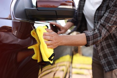 Photo of Man wiping car with yellow microfiber rag outdoors, closeup