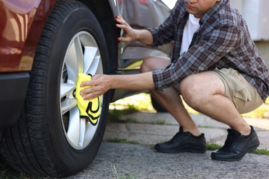Photo of Man wiping car wheel with yellow microfiber rag outdoors, closeup