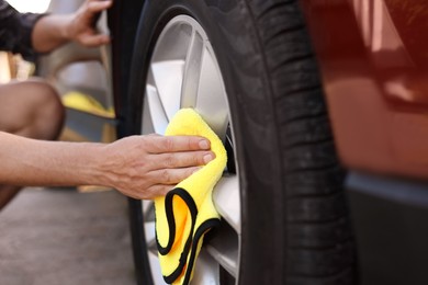 Photo of Man wiping car wheel with yellow microfiber rag outdoors, closeup