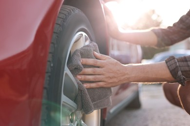 Photo of Man wiping car wheel with grey microfiber rag outdoors, closeup