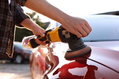 Photo of Man polishing car with orbital polisher outdoors, closeup