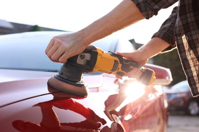 Photo of Man polishing car with orbital polisher outdoors, closeup