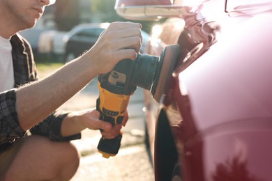 Photo of Man polishing car with orbital polisher outdoors, closeup